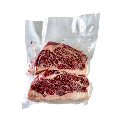 Two pieces of raw steak in a vacuum-sealed package on a white background
