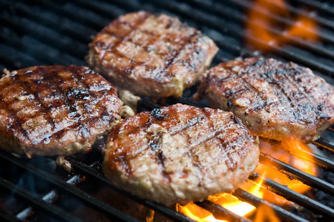 Three hamburgers cooking on a grill with flames below