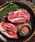 Two raw steaks on a dark plate with herbs and spices on a rustic background