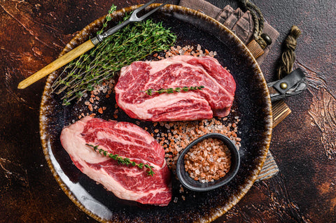 Two raw steaks on a dark plate with herbs and spices on a rustic background