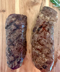 Two grilled steaks on a wooden cutting board with rosemary.