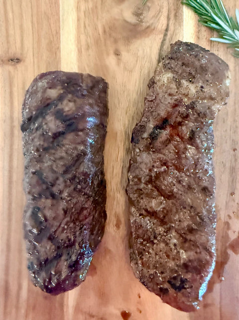 Two grilled steaks on a wooden cutting board with rosemary.
