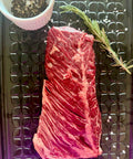 Raw beef ribeye steak on a metal surface with rosemary and pepper.