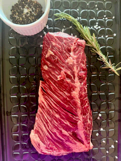 Raw beef ribeye steak on a metal surface with rosemary and pepper.