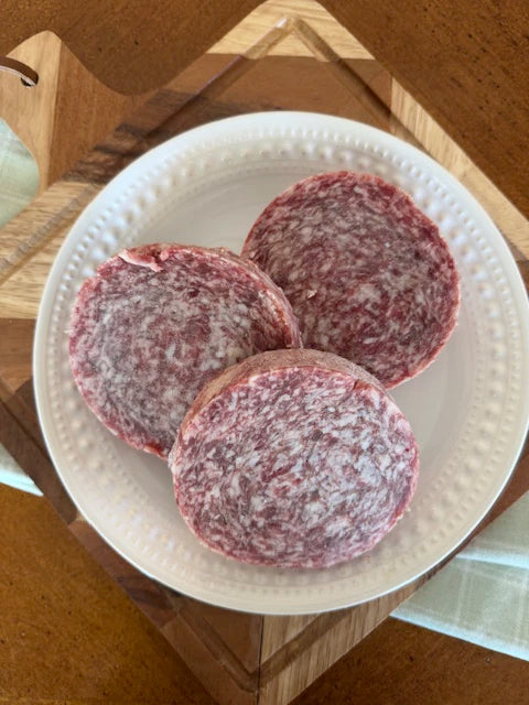 Three raw hamburger patties on a white plate with a wooden surface underneath.