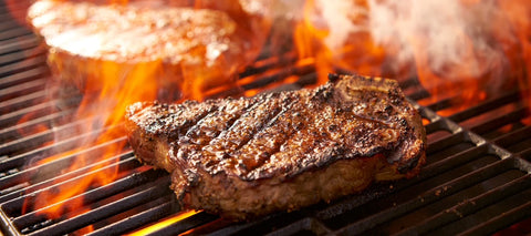 Steak being grilled over flames on a barbecue grill