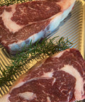 Two raw steaks on a metal surface with rosemary sprigs.