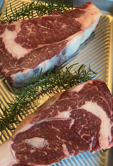Two raw steaks on a metal surface with rosemary sprigs.