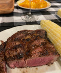 Steak and corn on the cob on a plate with a checkered tablecloth in the background