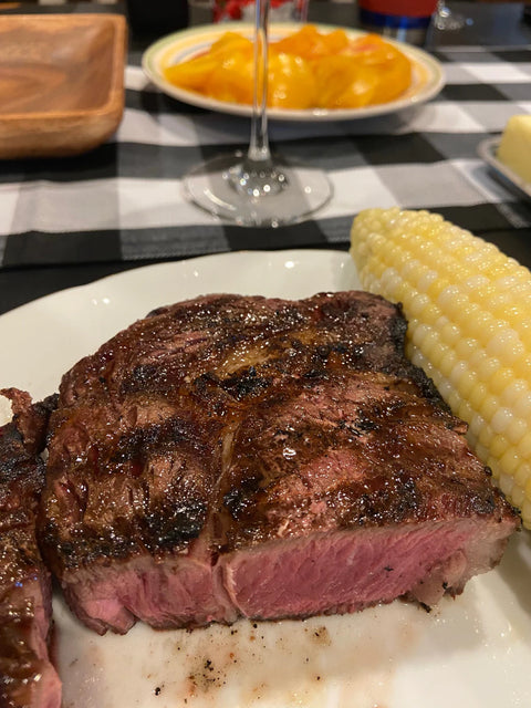 Steak and corn on the cob on a plate with a checkered tablecloth in the background