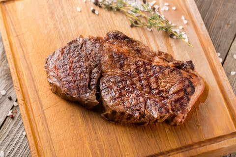 Grilled steak on a wooden cutting board with herbs