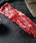 Raw steak on a dark surface with a knife and spices