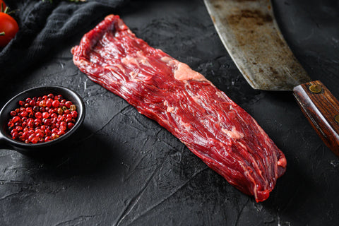 Raw steak on a dark surface with a knife and spices