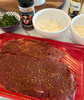 Marinated meat on a pink cutting board with seasonings and ingredients in the background.