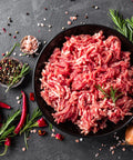 Ground meat on a black plate with red peppers, rosemary, and a spoon on a dark surface.