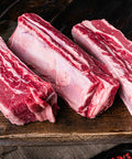 Three pieces of raw beef short ribs on a wooden cutting board.