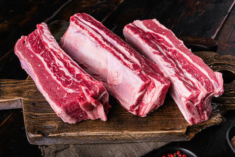 Three pieces of raw beef short ribs on a wooden cutting board.