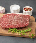 Raw steak on a wooden cutting board with garlic, salt, and peppercorns on a gray background