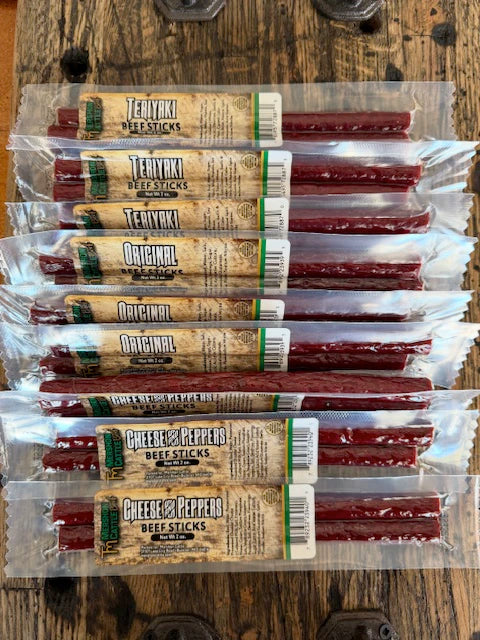 Multiple packages of beef sticks with a mixture of different flavors like Original, Teriyaki and Cheese and Peppers on a wooden surface