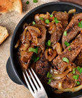 Fried beef with onions and herbs in a black bowl with bread on the side.