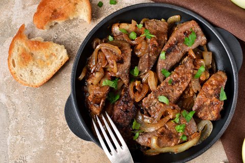 Fried beef with onions and herbs in a black bowl with bread on the side.