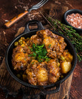 Stewed meat with potatoes and vegetables in a black skillet on a wooden surface.