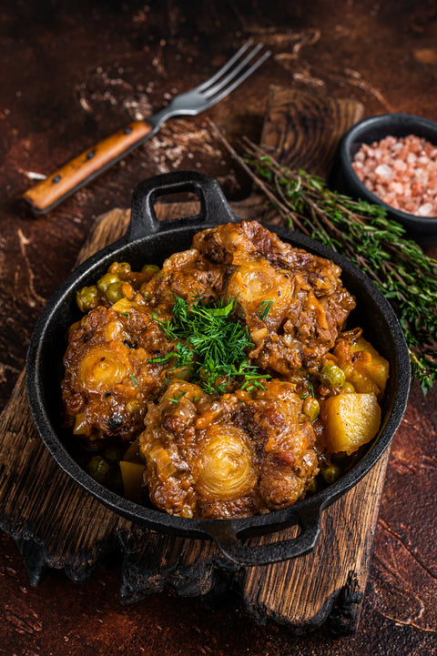 Stewed meat with potatoes and vegetables in a black skillet on a wooden surface.