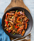 Fried beef with vegetables in a black bowl on a wooden cutting board.