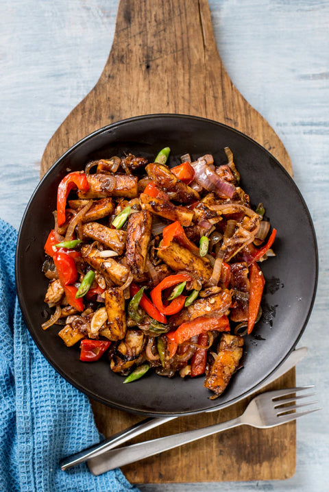 Fried beef with vegetables in a black bowl on a wooden cutting board.