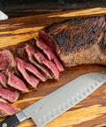 Beef tri-tip cooked and sliced on a wooden cutting board next to a knife