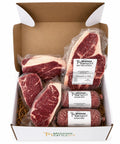 A boxed meat gift set from Mershon Cattle Co. containing four beef steaks and three ground beef sausages, all vacuum-sealed and arranged inside an open white and brown cardboard box on a white background.