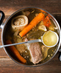 Pot of beef broth with vegetables on a wooden surface