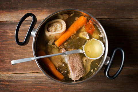 Pot of beef broth with vegetables on a wooden surface