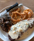 Plated meal with steak, onions rings, and mushrooms on a white plate.