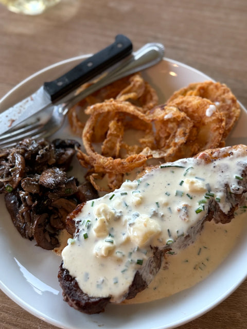 Plated meal with steak, onions rings, and mushrooms on a white plate.